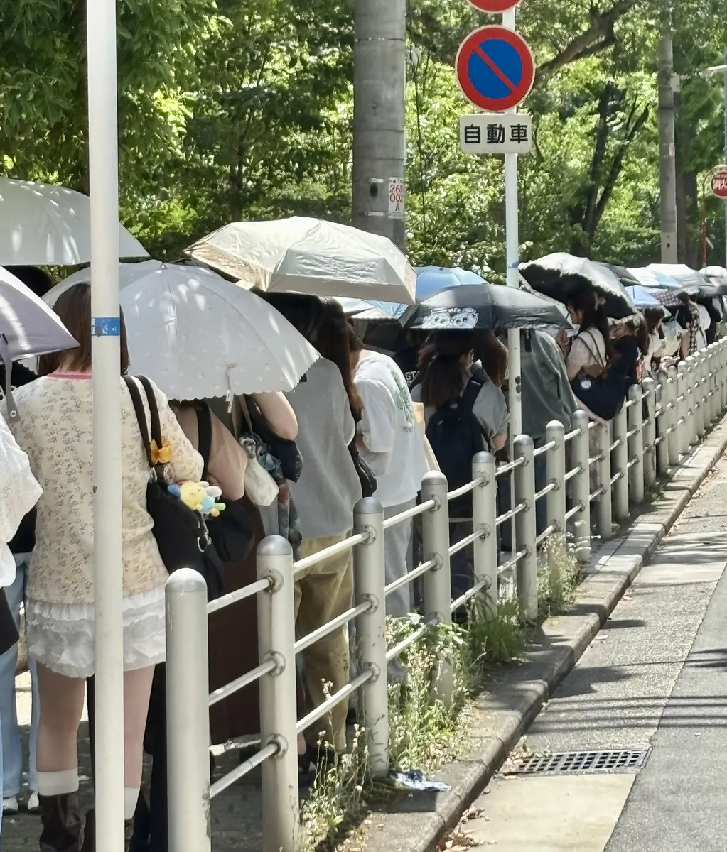 炎天下で日傘を差して並ぶ人たち